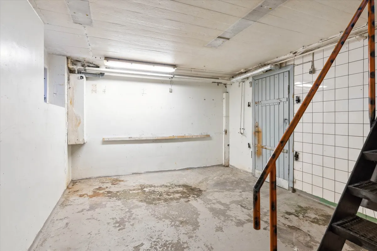 En gammel trappe fører op til en hvid, tom, fugtig kælder med et hul i væggen og en række hvide kakel.