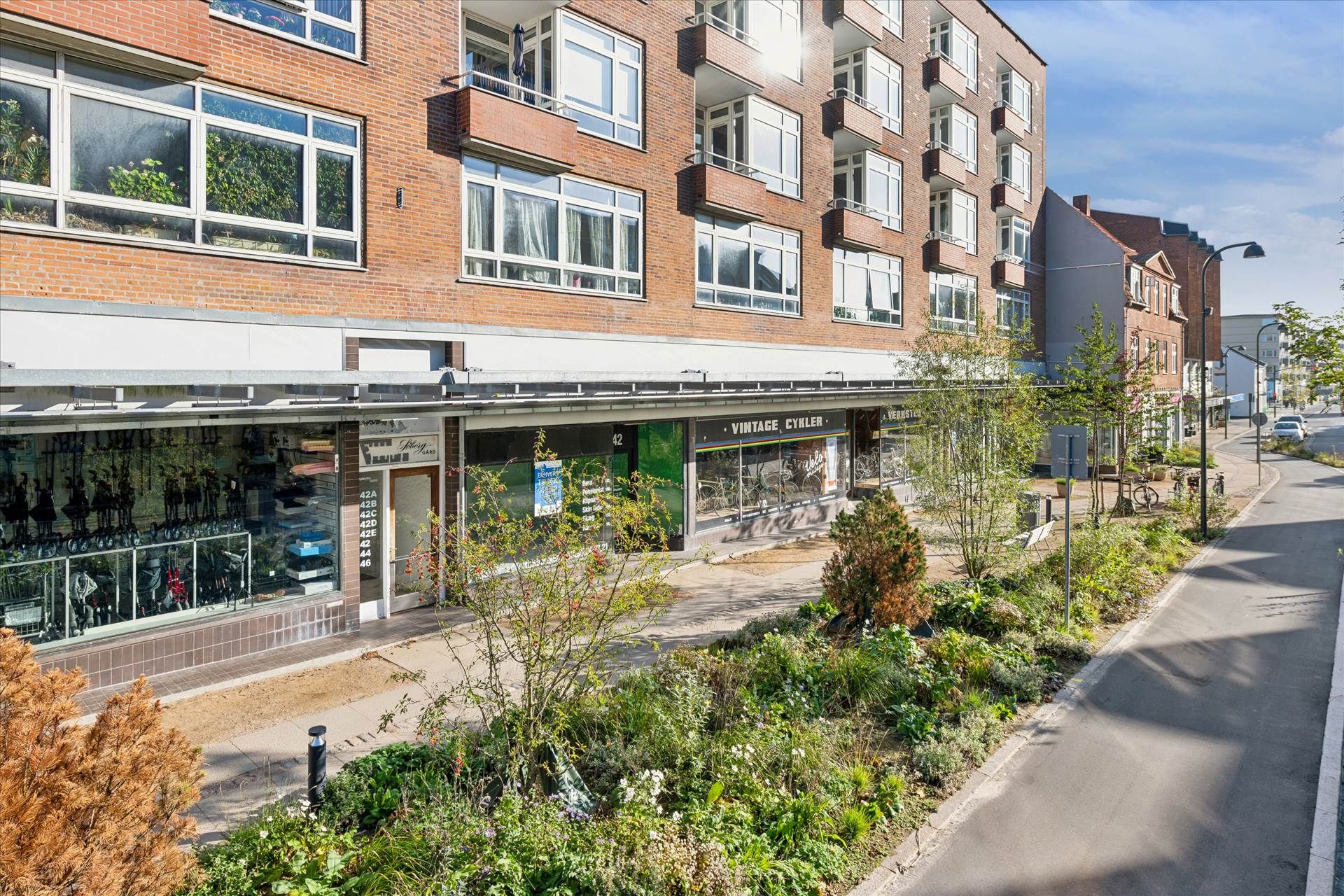 En nybygget forretningsbygning med flere butikker og lejligheder på Søborg Hovedgade, foran parkerede biler og grønne anlæg