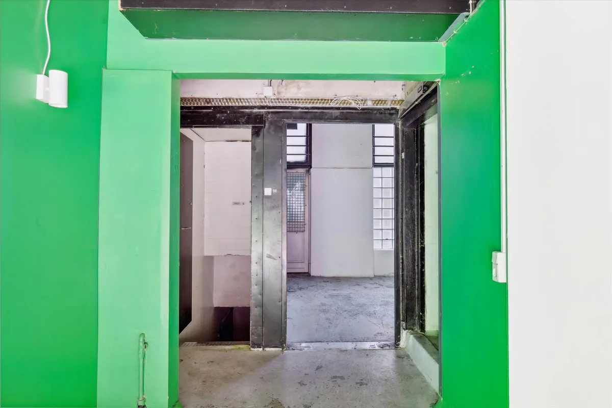 En åben dør i en grøn kælder med et lyserødt lys over højre side og en hvid væg til højre