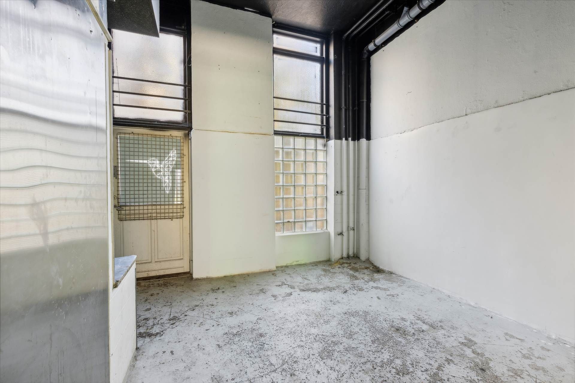 En tom, gammel forretningslokal, med hvide vægge og smuttende loft, og flere vinduer og døre, og en gammel elektriske