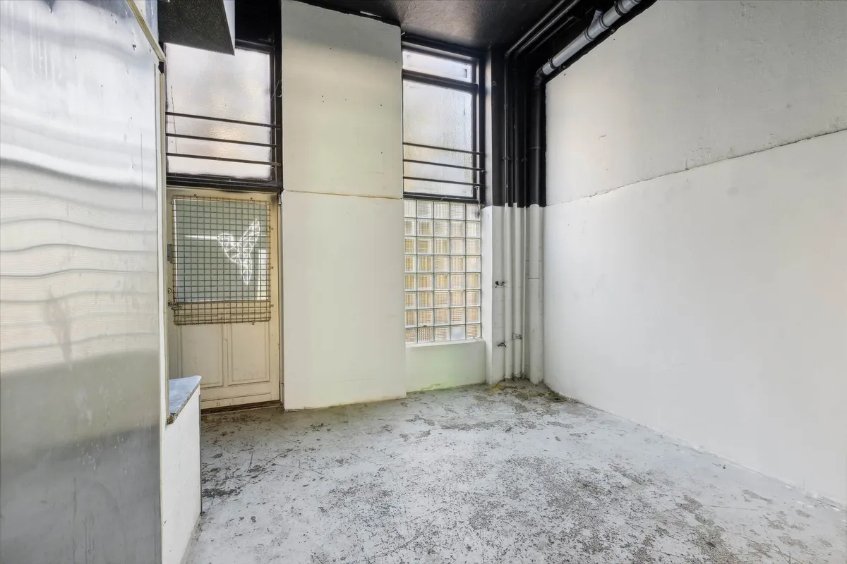 En tom, gammel forretningslokal, med hvide vægge og smuttende loft, og flere vinduer og døre, og en gammel elektriske