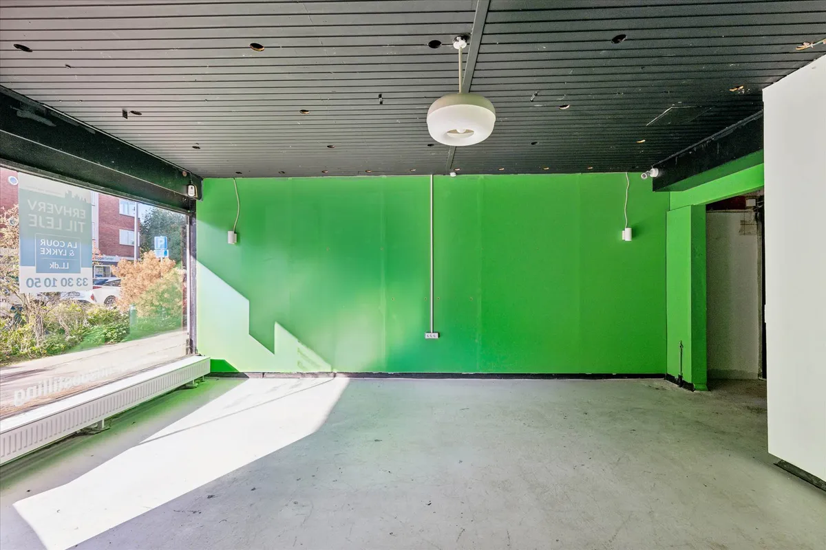 Lokaler til leje med store vinduer og grønne vægge, møbler og udstyr til venstre, solstråler på gulvet, to lysekroner og et