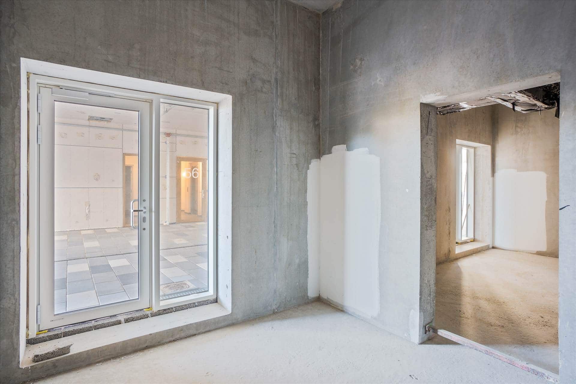 Et tomt rum med hvide vægge og glasdøre. Der er et hjørne med tørre vægge og højtloft. Der er en lille dør med et vindue i