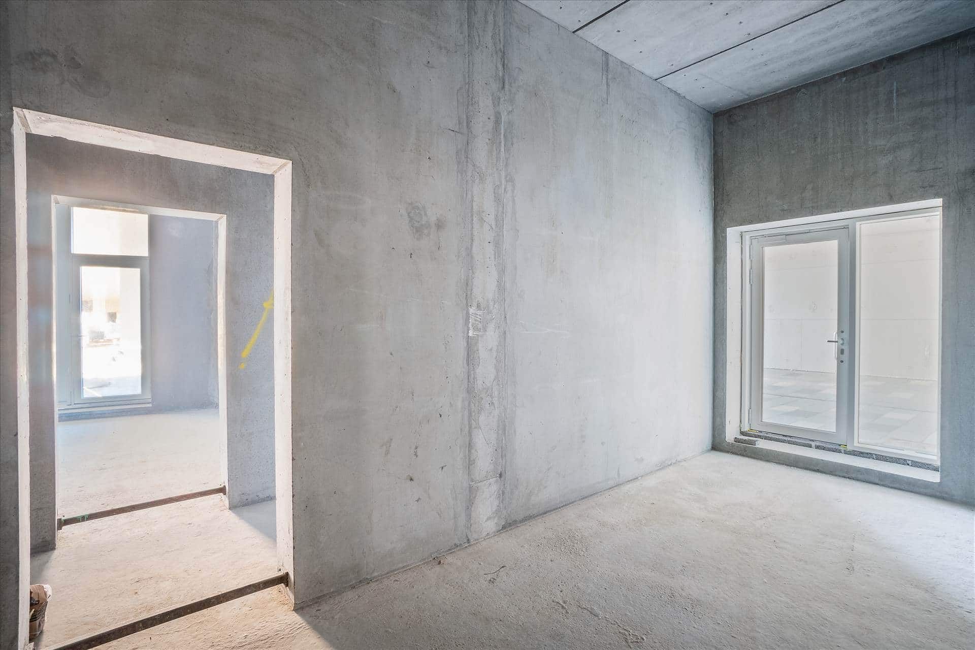 En tom stue med hvide vægge og gulv samt to vinduer og en dør. Et gult pilmærke er malet på den højre væg.