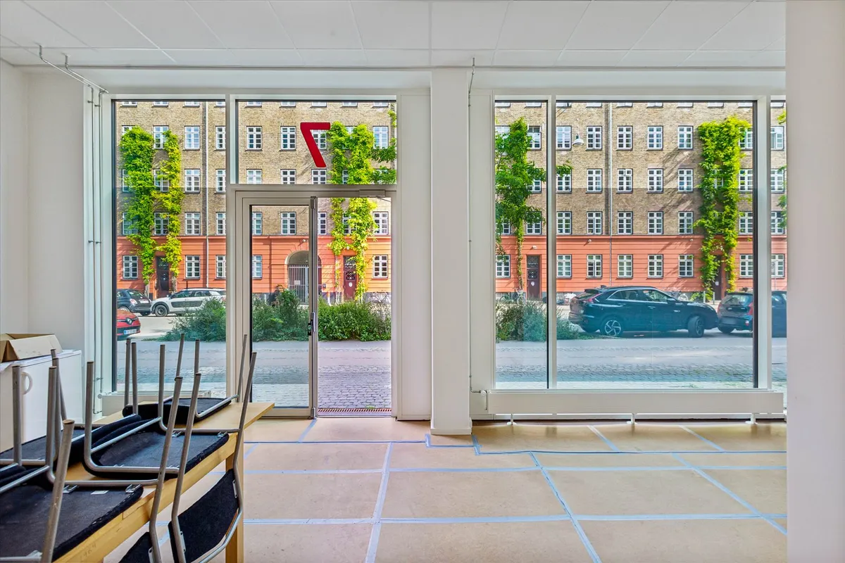 Store vinduer i moderne bygning med et rødt tal og flere biler parkeret udenfor