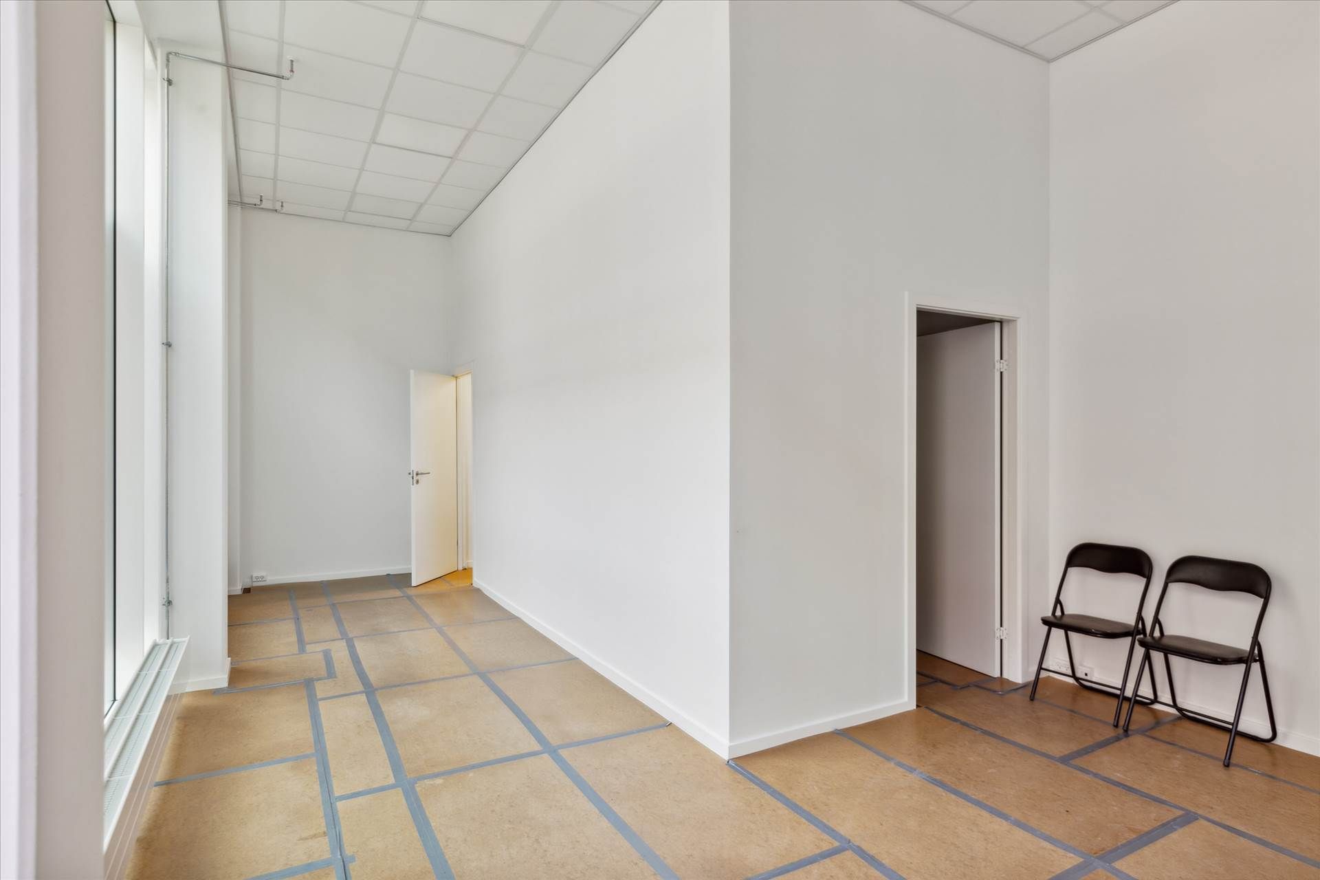 Et stort, renmalet rum med to stolpe stående og lyse gulve. Der er to stole samt åbne døre på siden.
