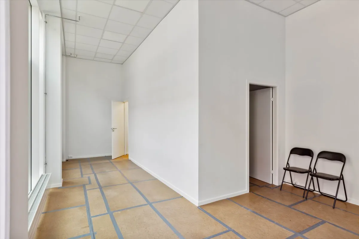 Et stort, renmalet rum med to stolpe stående og lyse gulve. Der er to stole samt åbne døre på siden.