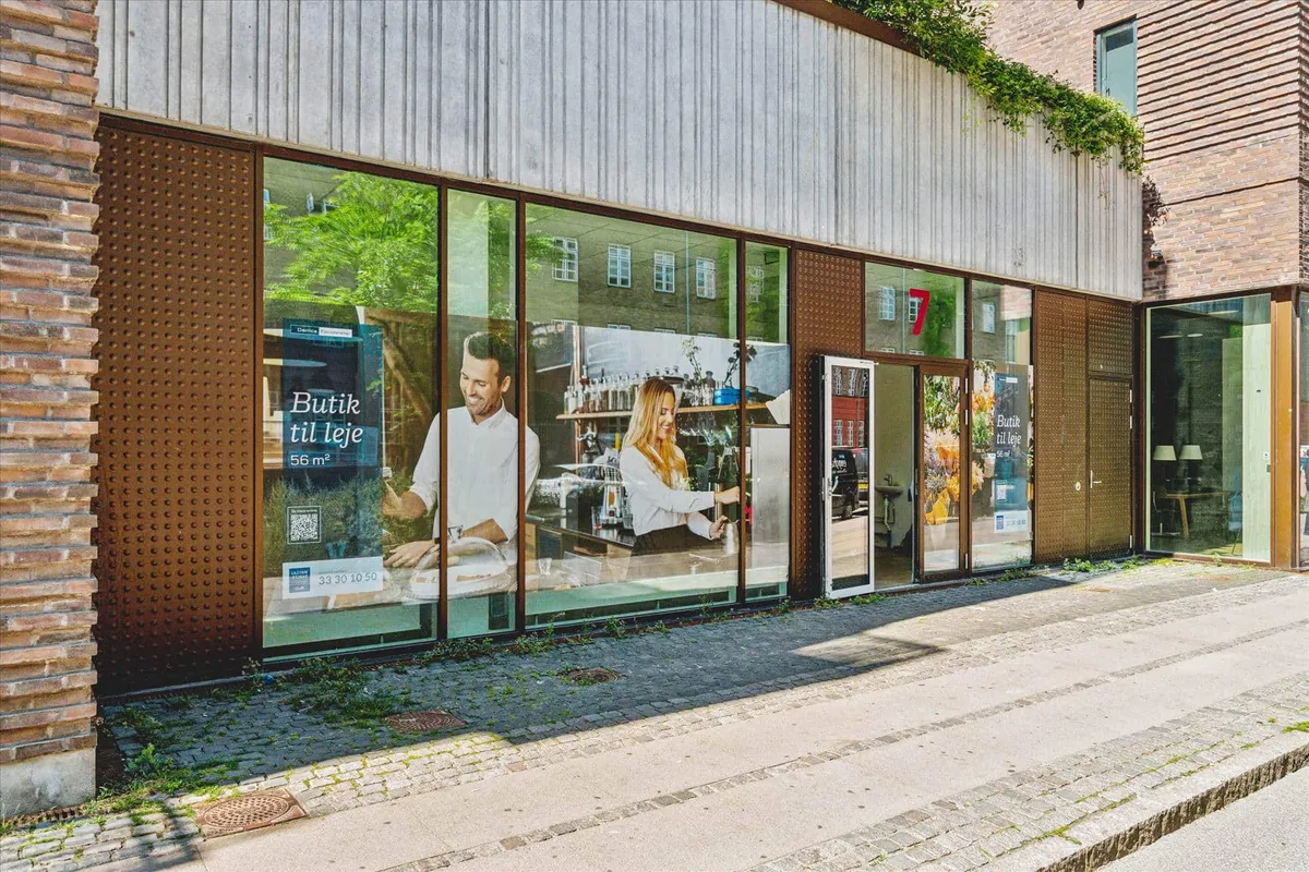 En 7-eleven med glassfront og åbne døre, hvor en mand og en kvinde står i spejlet.