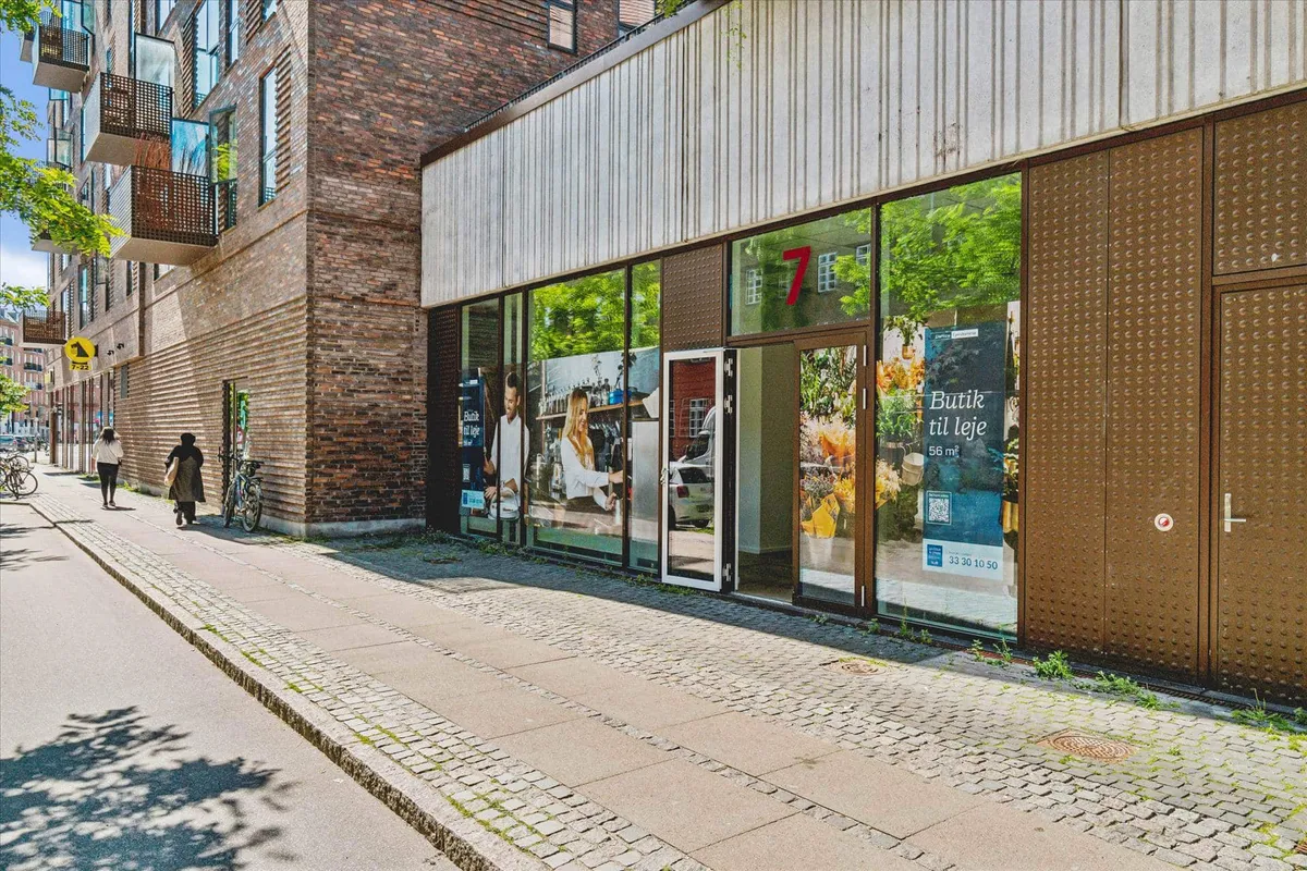 Mennesker går på gågaden udenfor et lille butikslokal med nummer 7 og reklame på de store vinduer