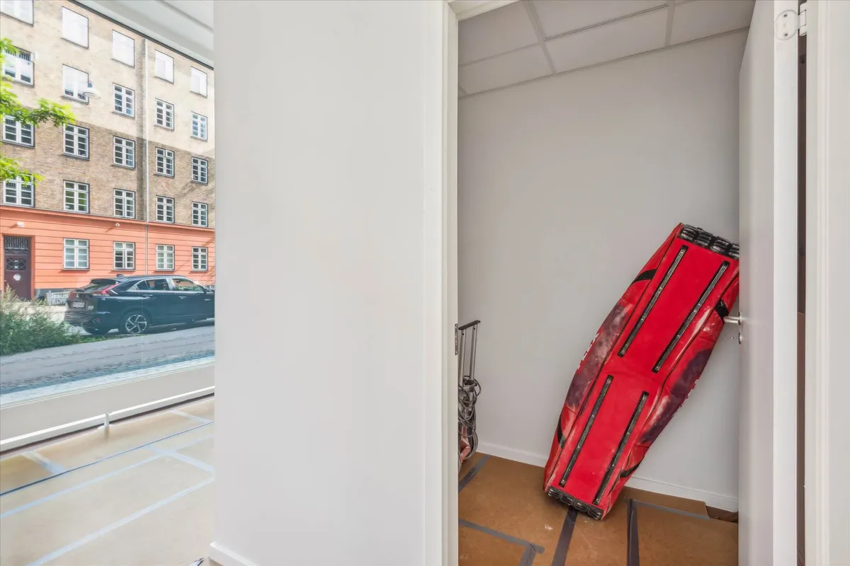 Et lille rum med en rød taske og en kufferte, hvor det er åbent og ud til en gade med biler og bygninger