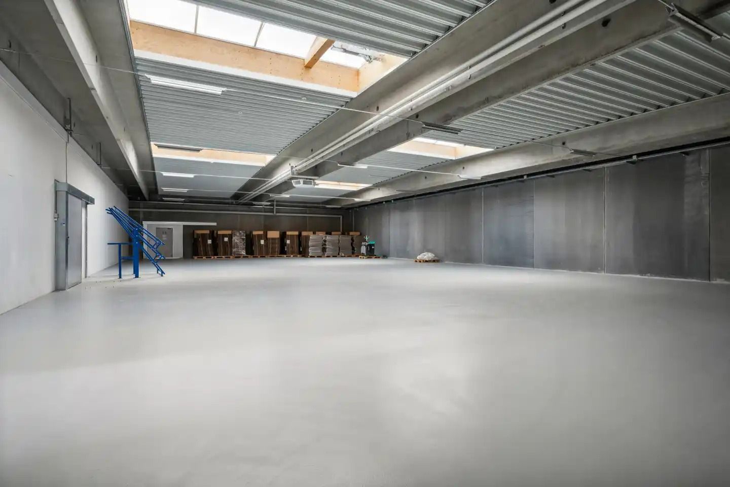 Inde i et stort lager er der en stor, tom og ren gulvfladesk. På den ene side er der en port og en lille stige