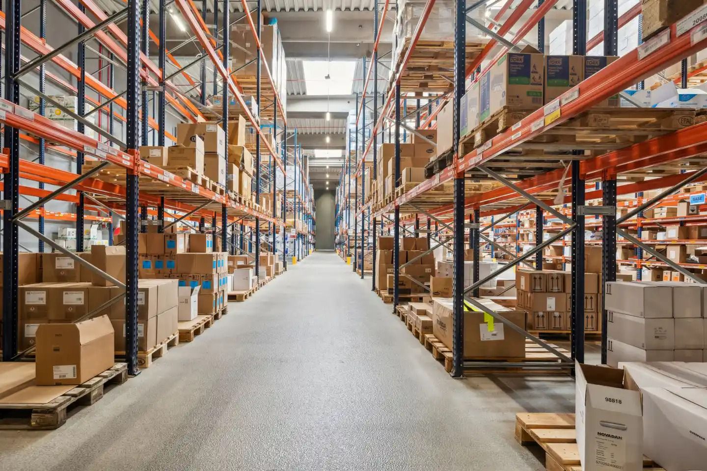 Lager med flere høje lagerhylder fyldt med forskelige kasser og bokse. Hylderne er forsynet med elektriske lys og det er