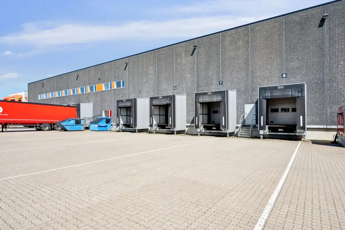 Et stort, gråt lagerhus med åbne portdøre og en stor rødslere parkeret foran