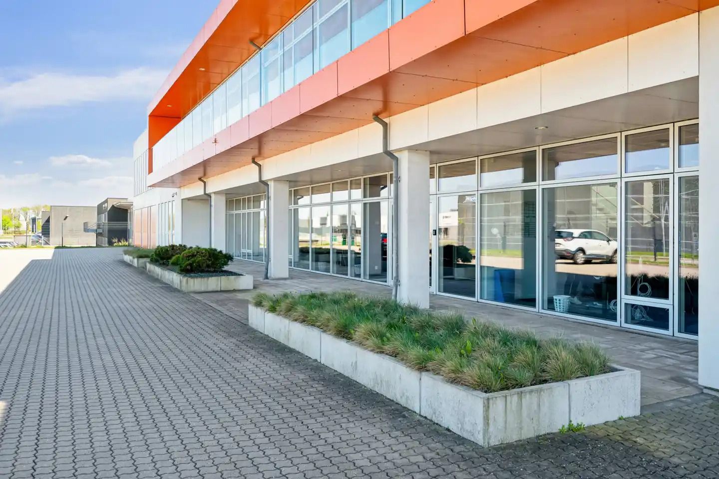 Foran bygningen er der en vej med grønne planter og to buske samt to skulpturer med græs og buske