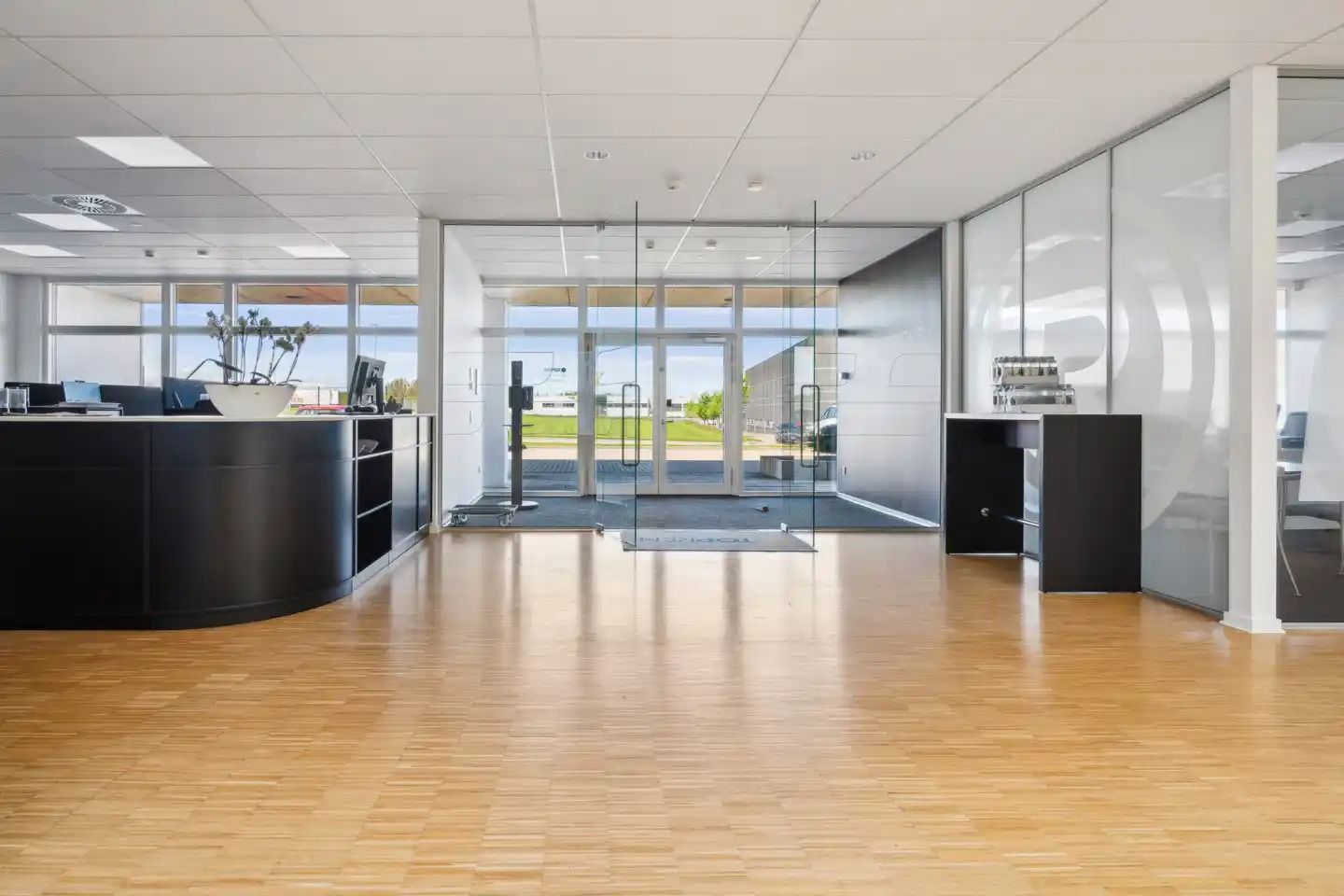 Indenfor er der en lobby med en høj reception, hvidt loft og gulv og glasdøre med en slank ramme