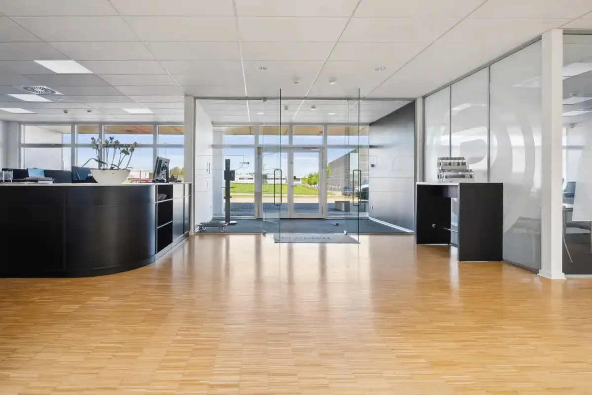 Indenfor er der en lobby med en høj reception, hvidt loft og gulv og glasdøre med en slank ramme