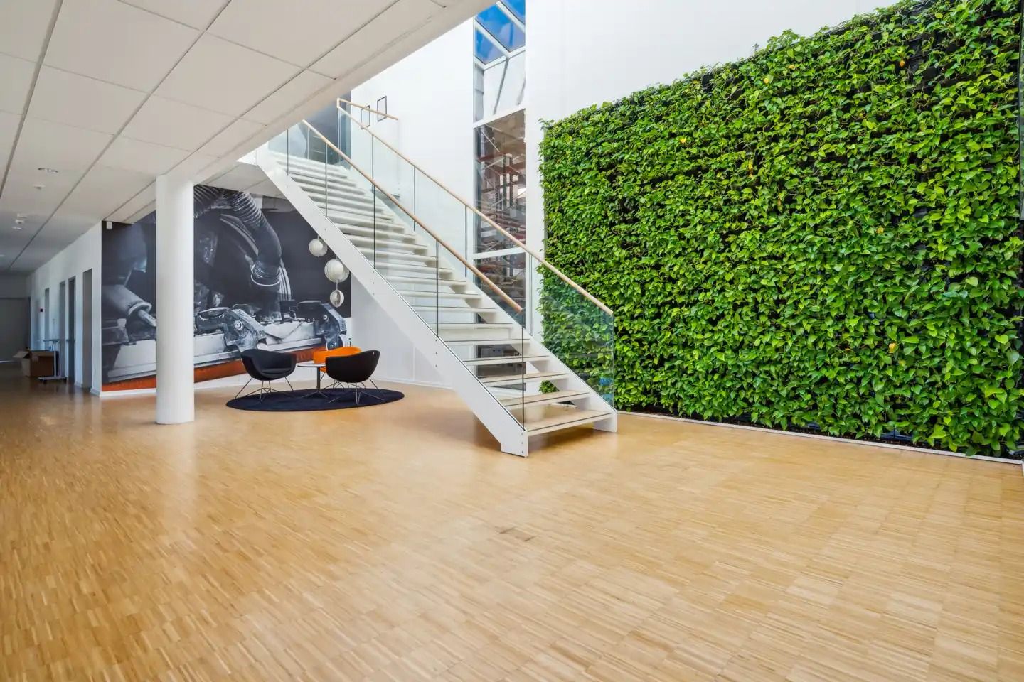 Køkken med moderne møbler og gulvbelægning, grønne planter på væggen, hvidt loft og gulv, og lyse vinduer