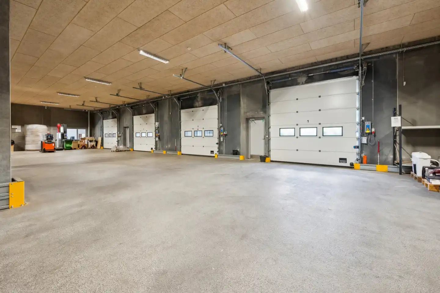 En stor, tom bygning med højt til lofts og hvide garageporte samt gul gulvmærkning og røde og hvide søjler