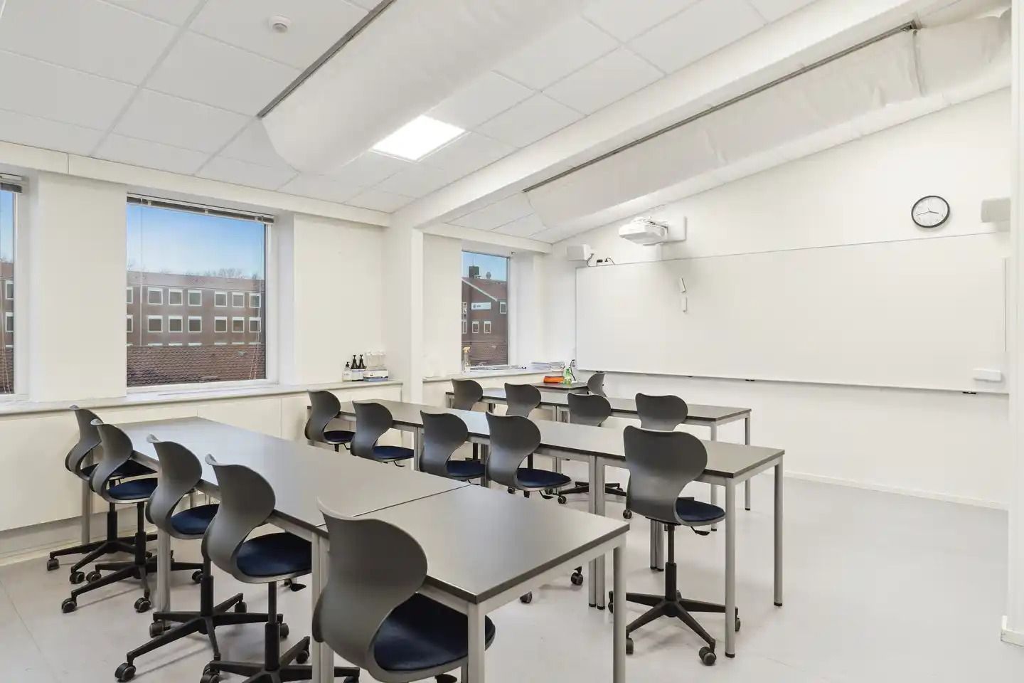 Klasselokal med hvide vægge og gulv, højt til loftet, vinduer og møbler i moderne stil og farve