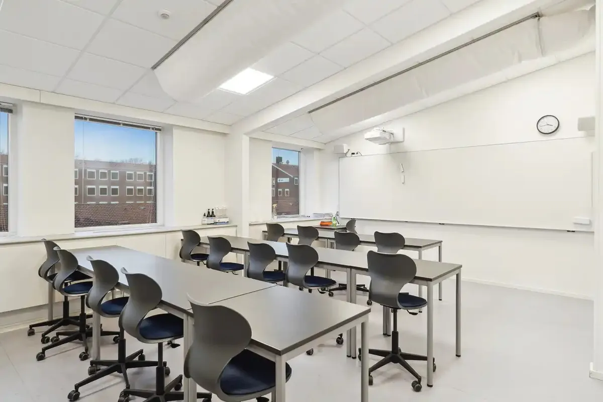 Klasselokal med hvide vægge og gulv, højt til loftet, vinduer og møbler i moderne stil og farve