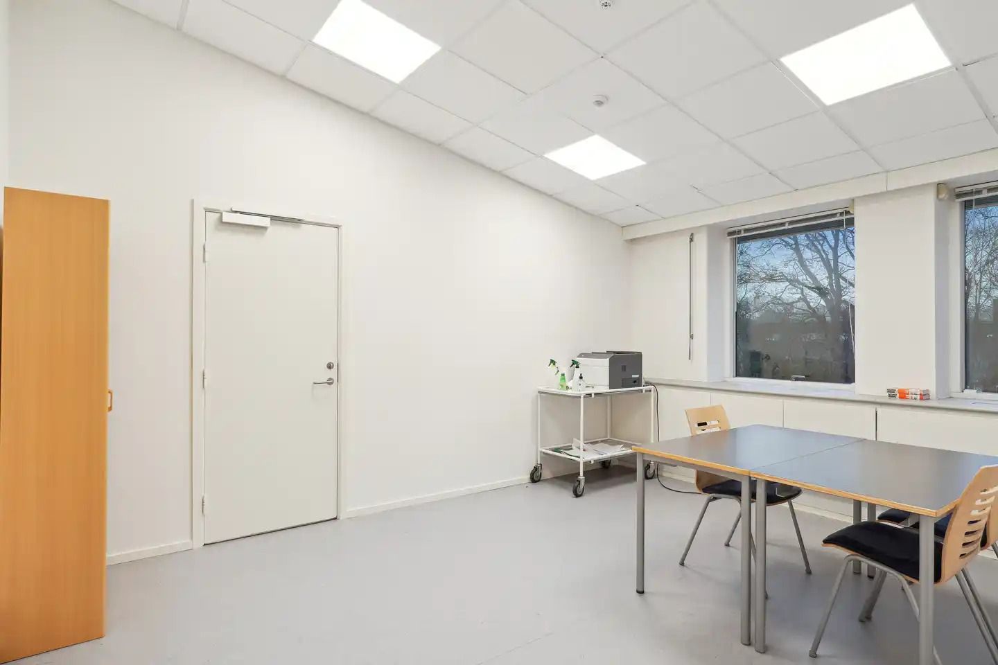 En tom kontor med hvide vægge og højloft med hvide loftspaneler, gulve og borde med stole samt en skrivemaskine og