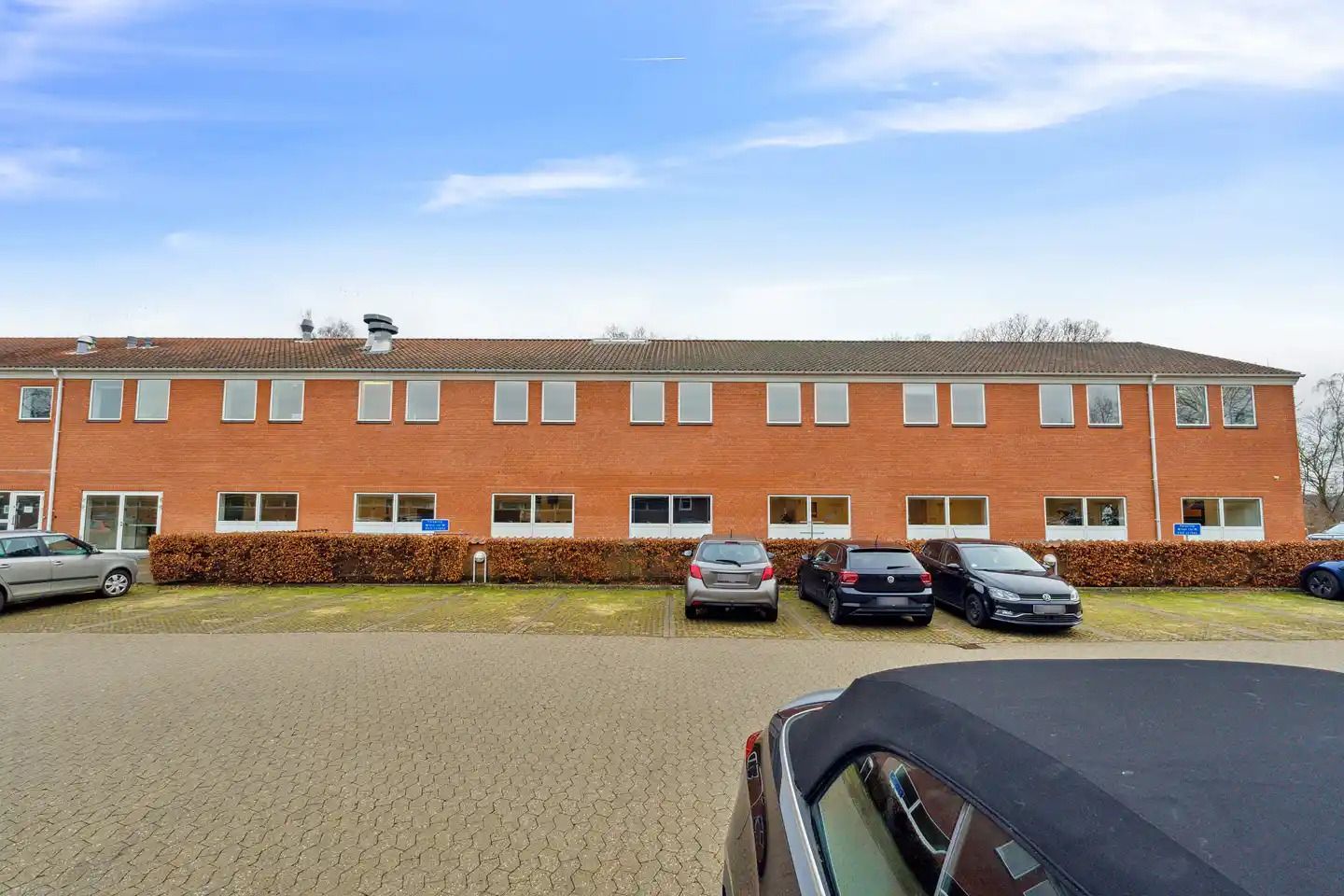 Biler parkeret i forskud for en orange bygning med mange vinduer og et fladt tag