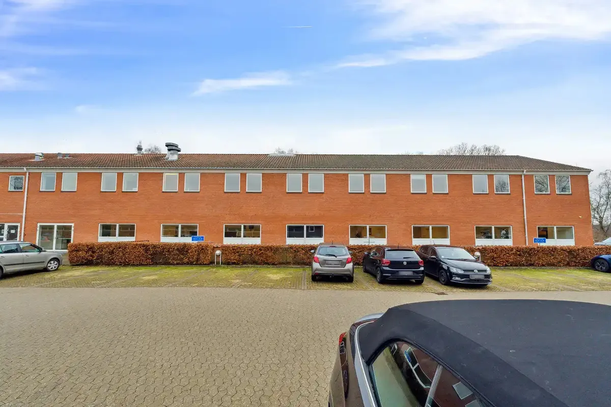 Biler parkeret i forskud for en orange bygning med mange vinduer og et fladt tag