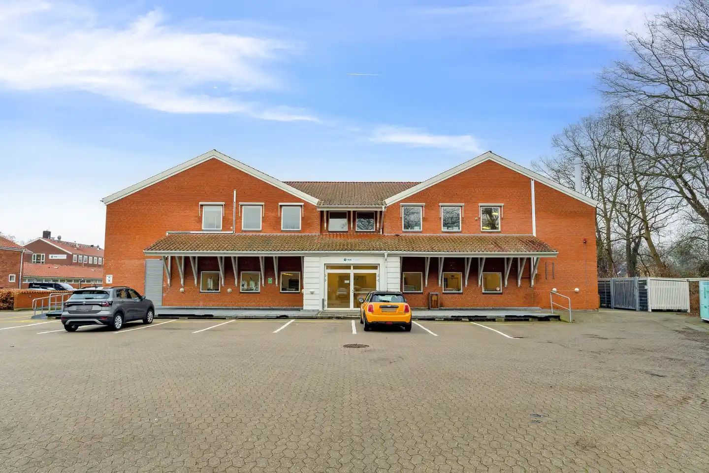 To biler parkeret foran en rødmalet bygning med flere vinduer og terrasse i Kongens Lyngby