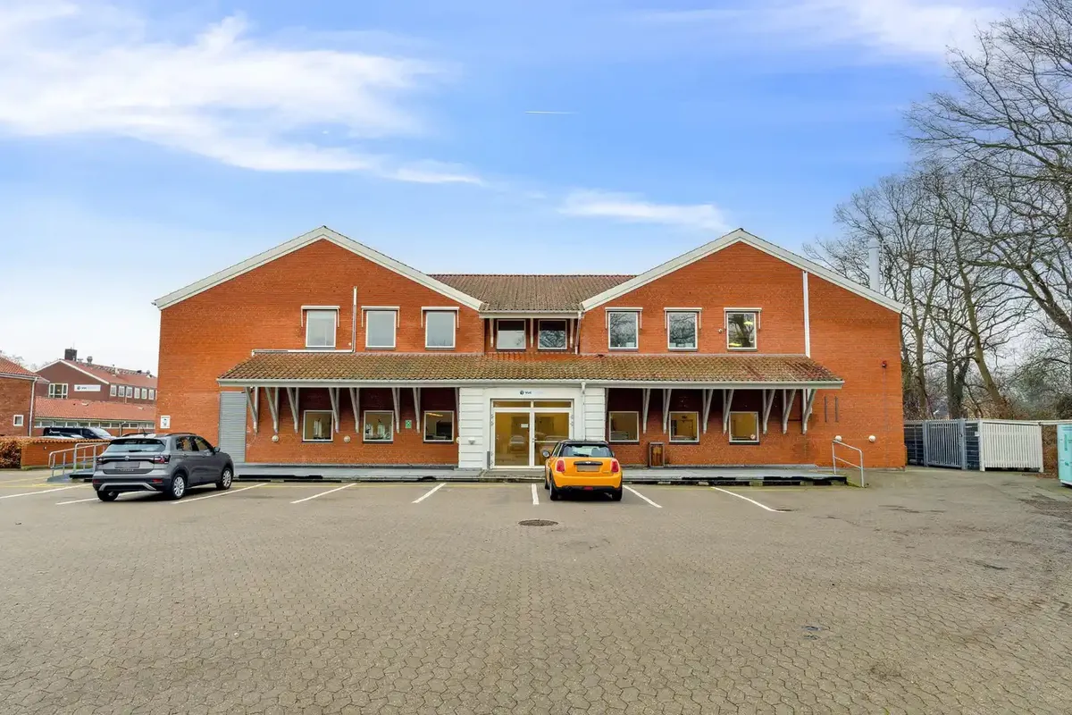 To biler parkeret foran en rødmalet bygning med flere vinduer og terrasse i Kongens Lyngby