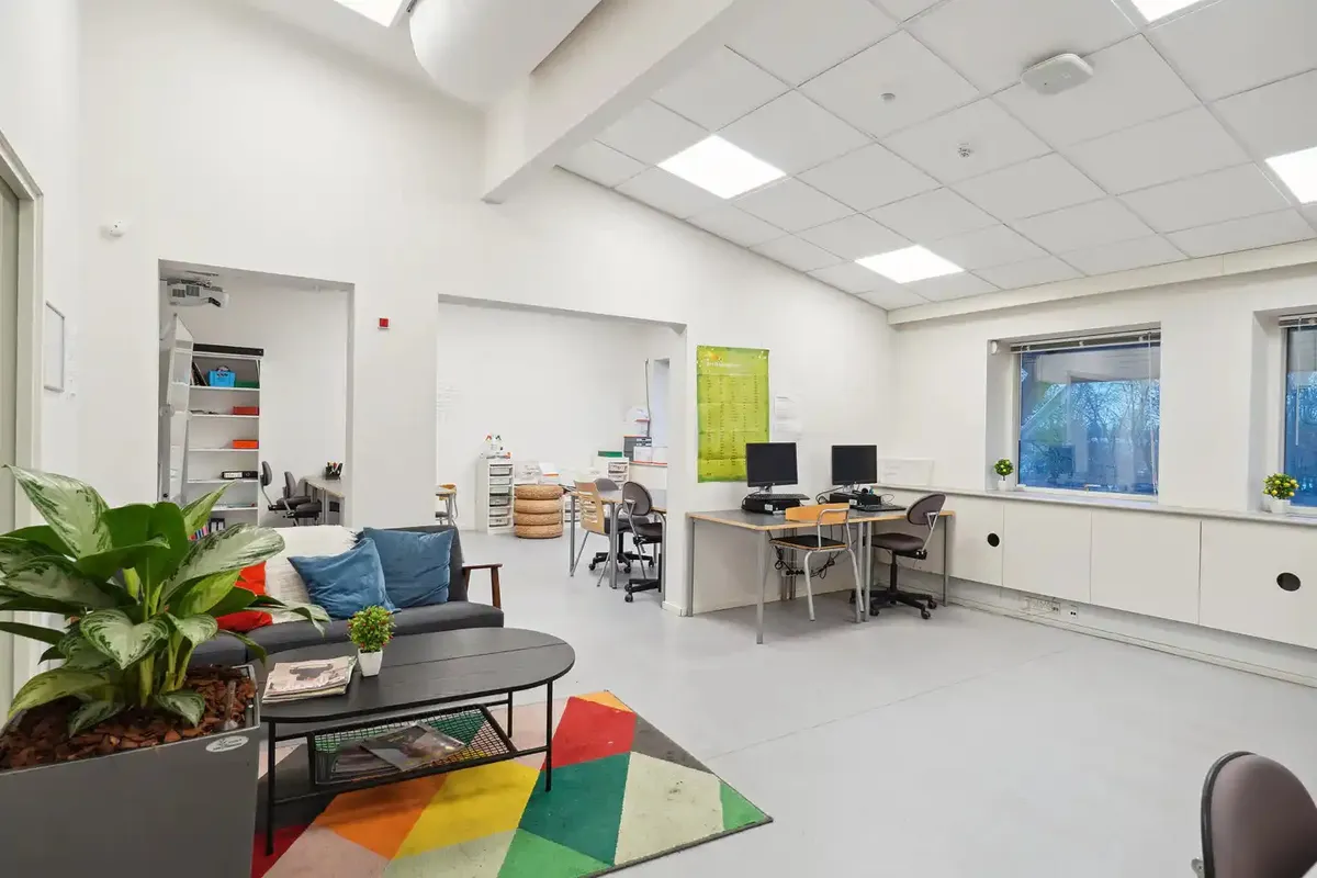 Kontorlokaler med moderne møbler og plante i hjørnet samt et skrivebord med computer og stol i baggrunden