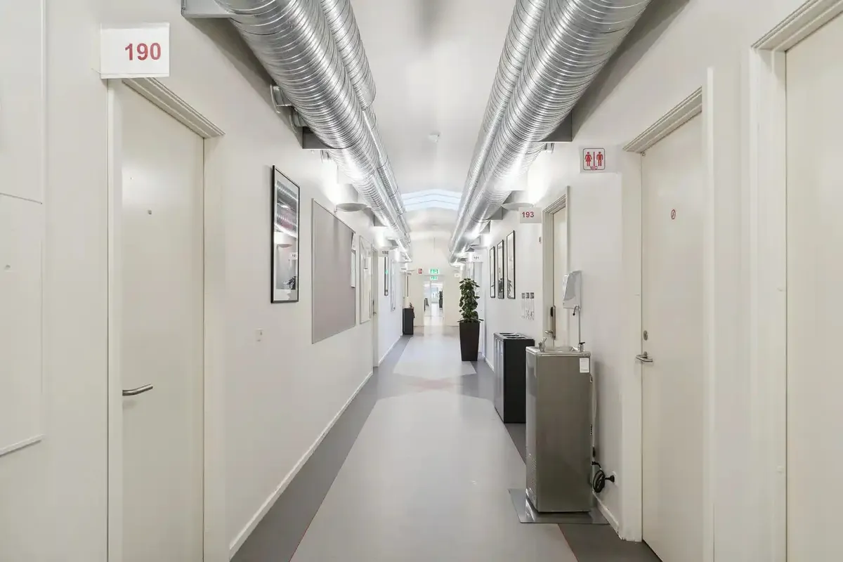 En række hvide døre og rummelige gange i en bygning med lyse lofter og gulvbelægning