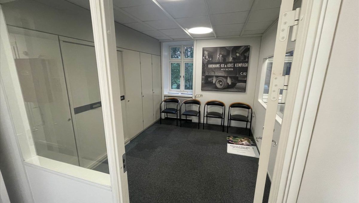 To kontorlokaler med lyse hvide vægge og en lyseblå gulv. Værelset har fire stole, en plakat og et vinduesparti.