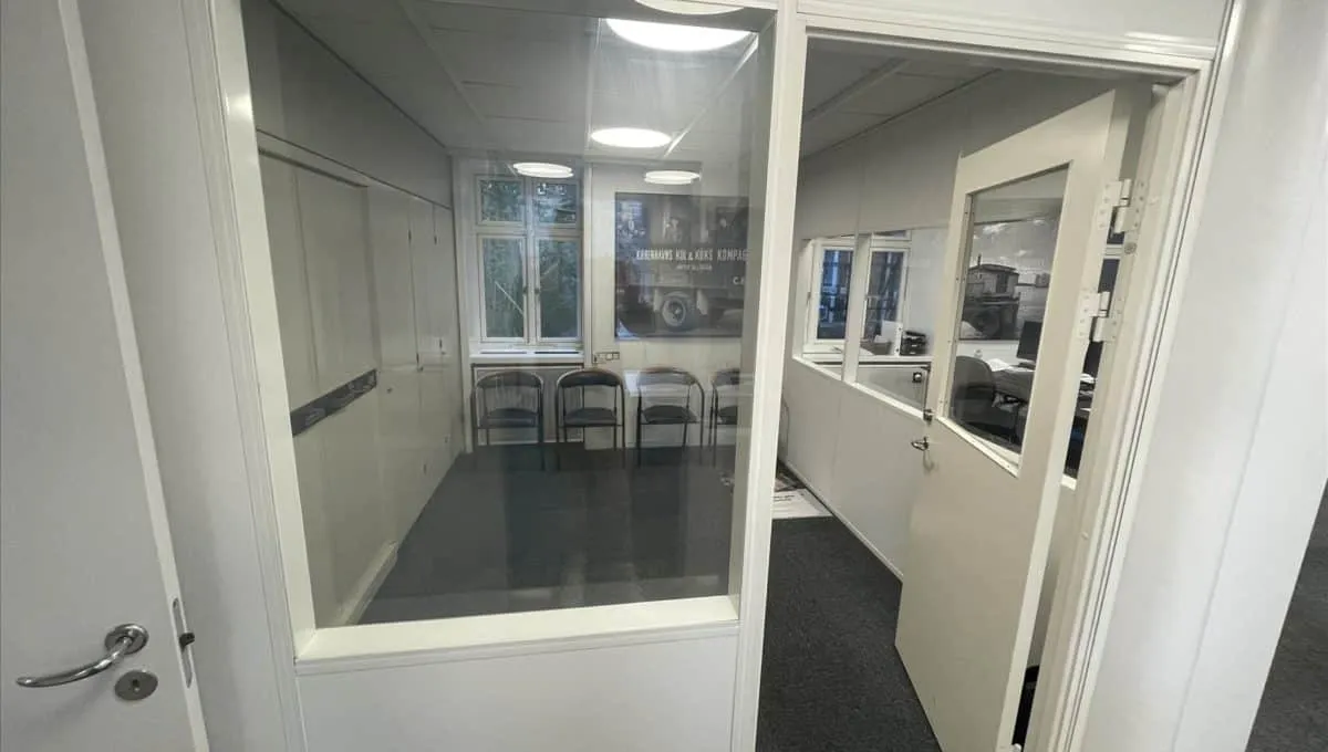 Glassdør med håndtag og åbne indgangsdøre til et moderne kontor med hvide vægge og lyse loftslamper