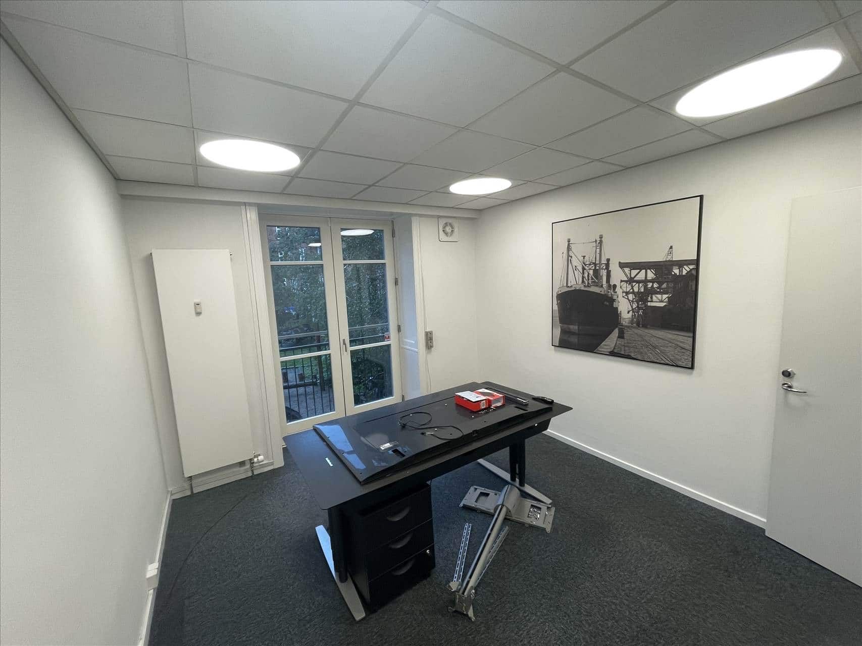 Kontorrum med højt loft og hvide vægge samt et bord med en tv og flere genstande placeret på gulvet