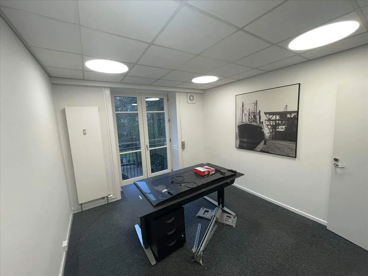 Kontorrum med højt loft og hvide vægge samt et bord med en tv og flere genstande placeret på gulvet