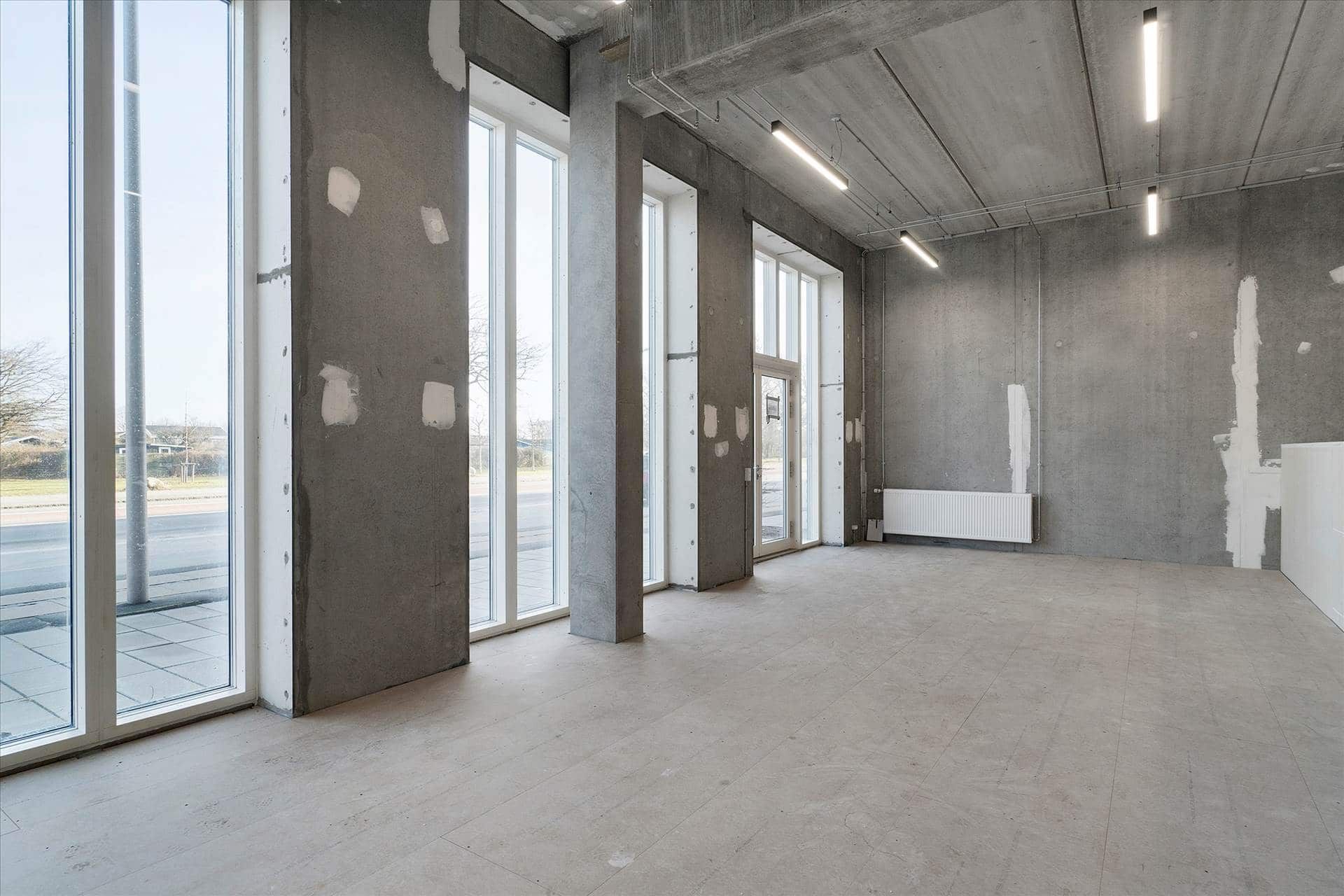 Store glasruder og lyse loftsbelysning i erhvervslokaler på Amager Strandvej med en stor indgangsdør og en hvid radiator.