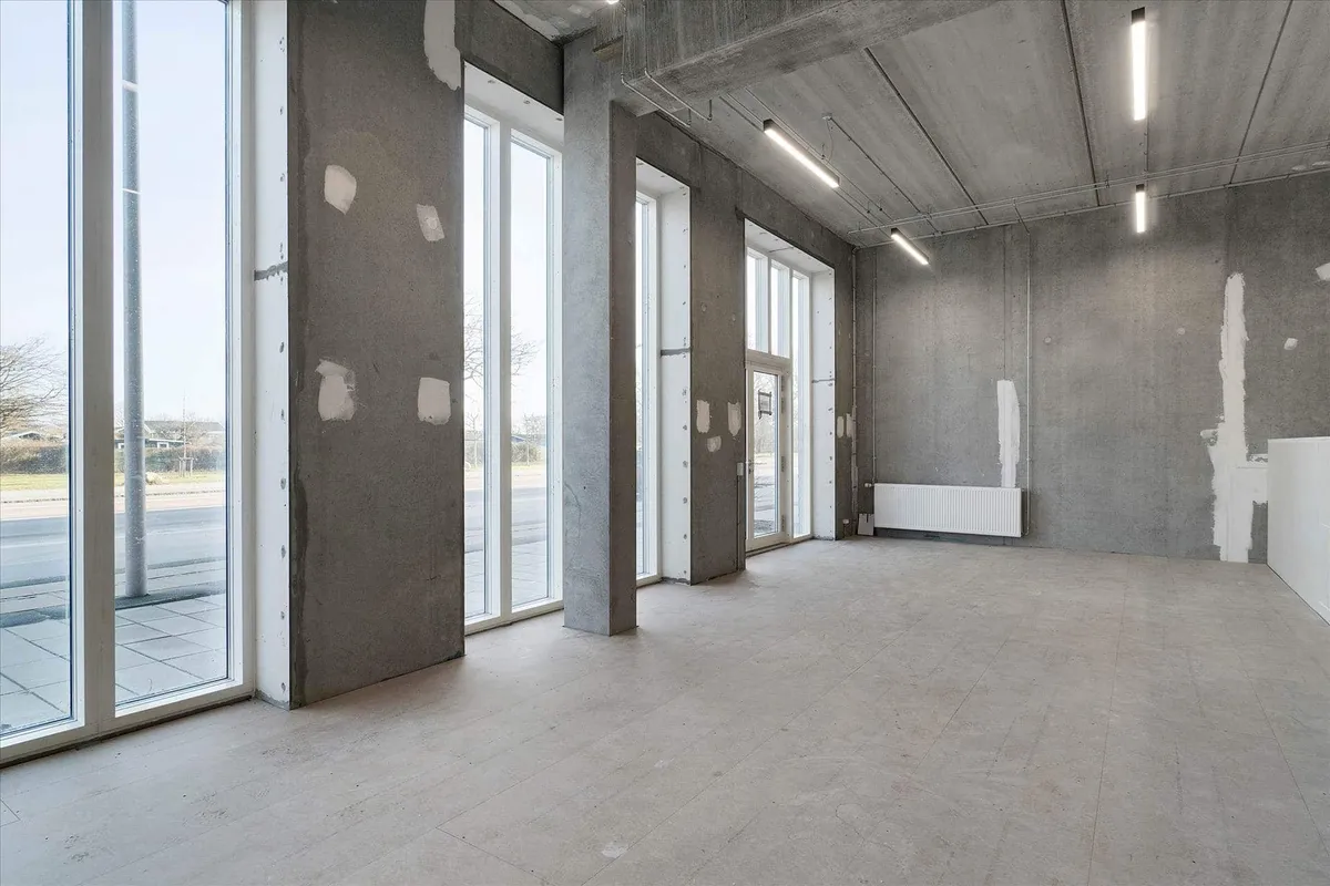 Store glasruder og lyse loftsbelysning i erhvervslokaler på Amager Strandvej med en stor indgangsdør og en hvid radiator.