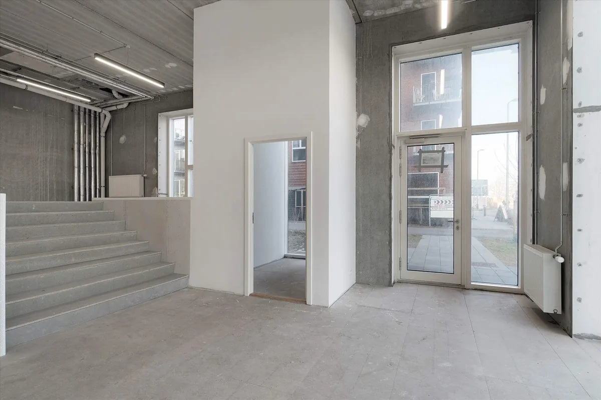 Styrket gulv, glasdøre og trapper, lyse lofter, ventiler og en åben indgang, der fører til en gårdhave med grønne planter og