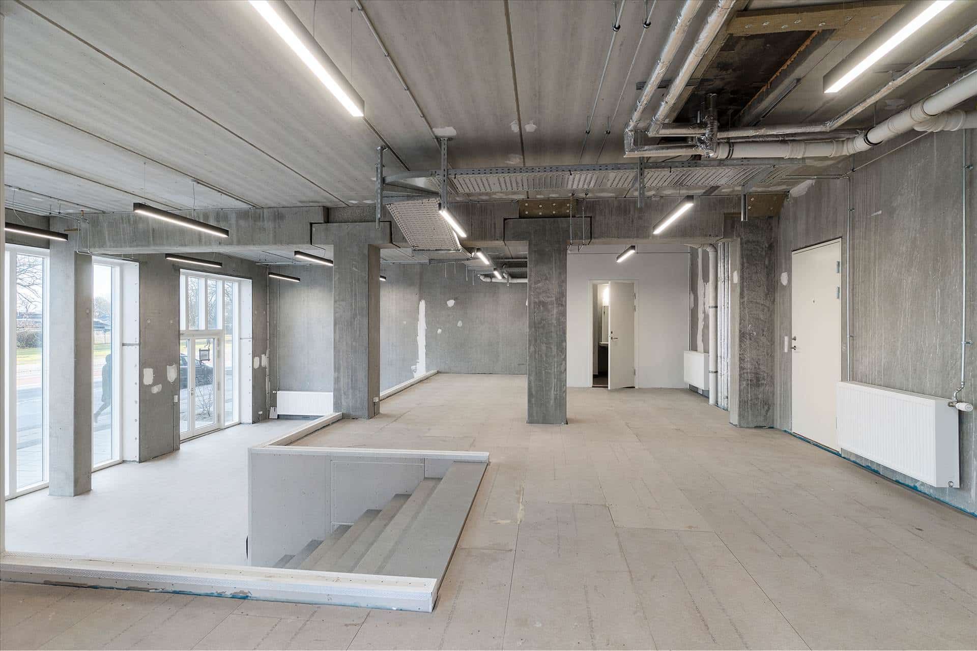 En stor, tom bygning med masser af vinduer, højt loft, tærskler og jordgulv og en hvid trappe.