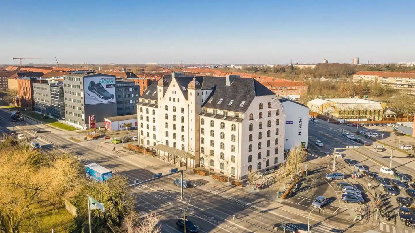 Kontorbyggeri med flere biler i kø, flere vinduer og en Hitachi-reklame.