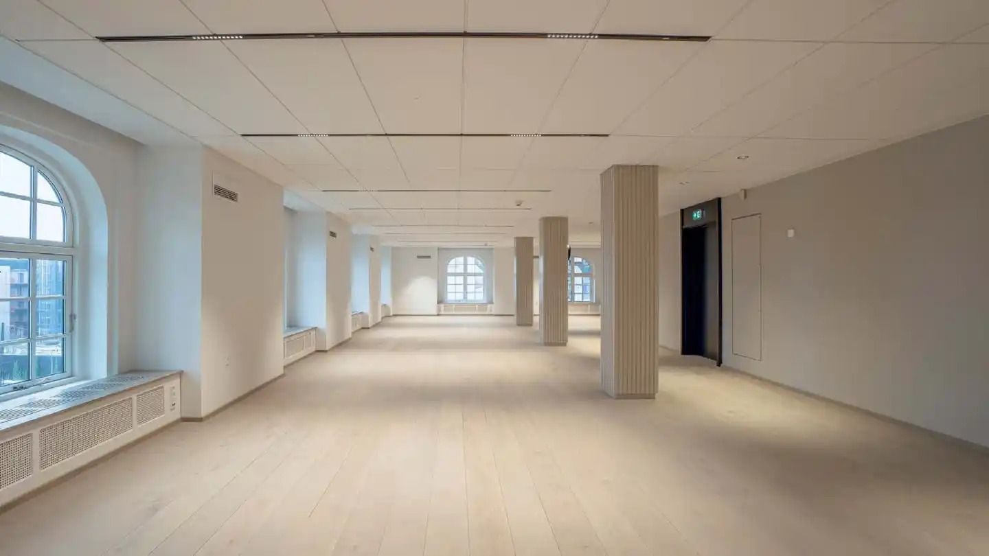 Elegant og rummelig korridor med hvide vægge, højt loft, lysevinduer og parketgulv