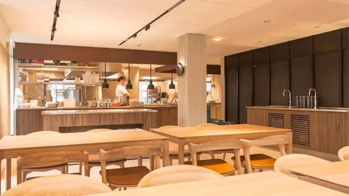 Kontorlokaler med moderne design og træmøbler, en person i køkkenområdet og to vandhaner på en køkkenvæg