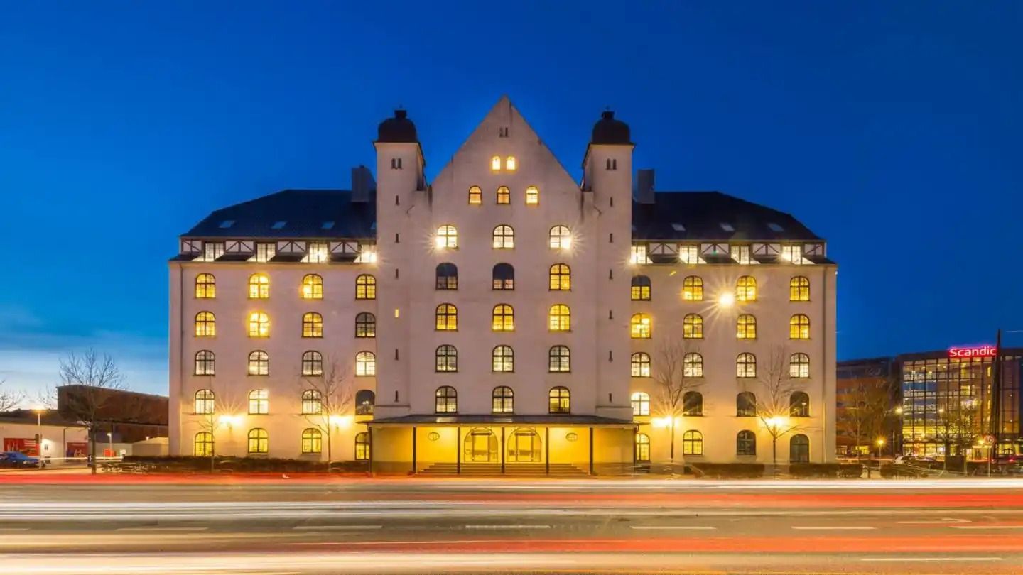 Store hotel med lys i alle vinduer, mørke gader og biler i baggrunden