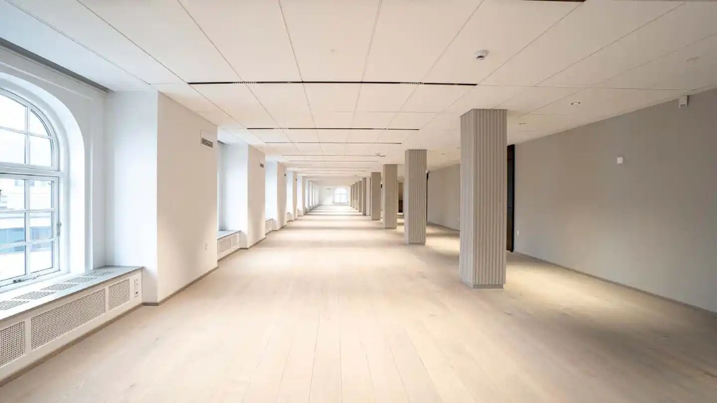 En lang korridor med hvide vægge, gulve og loft med søjler i midten og lyseruder med udsigt til byen