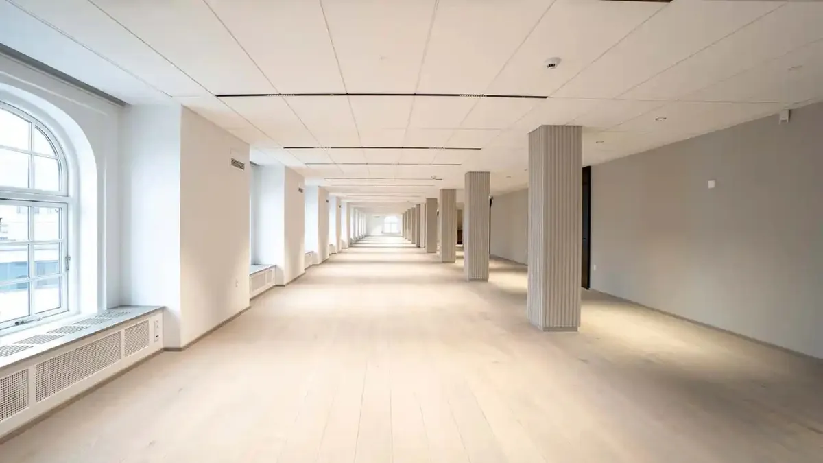 En lang korridor med hvide vægge, gulve og loft med søjler i midten og lyseruder med udsigt til byen