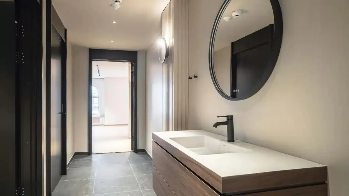 Elegante kontorlokaler med dobbeltvask og spejl samt åbne døre og hvid væg med lysepunkter