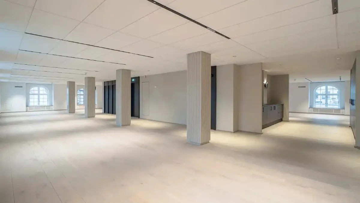 Kontorlokaler med lyse lofter, hvide vægge og hvidt gulv med lyse accenter. Store vinduer og høje søjler i lokalet