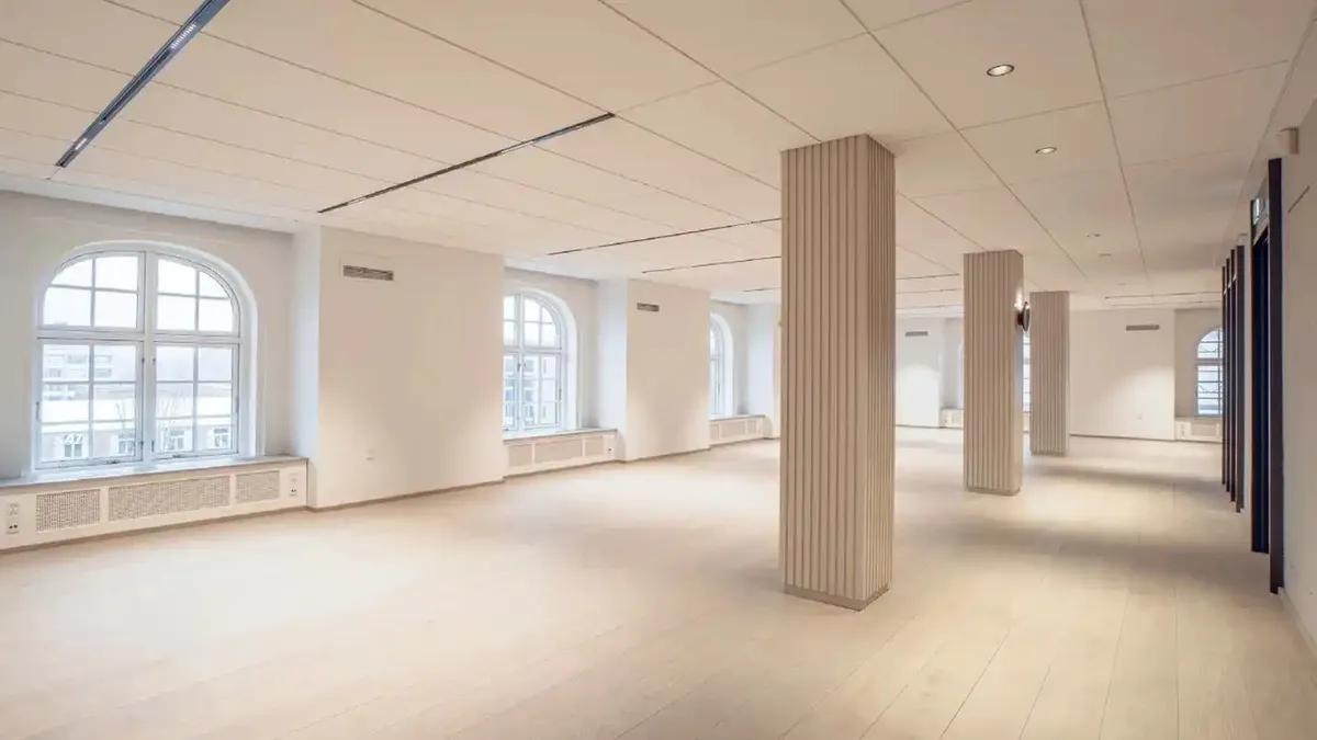En stor, lys og ren kontorlokal med hvide vægge og loft, tre høje søjler og store vinduer