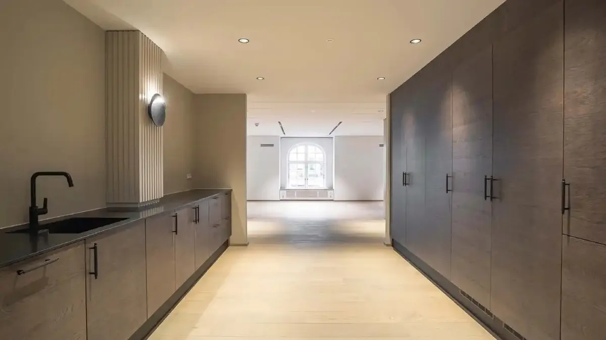 Minimalistisk køkken med moderne design, hvid væg, højloft og store vindu. Sort blækspruttekran og grå skabe med håndtag,