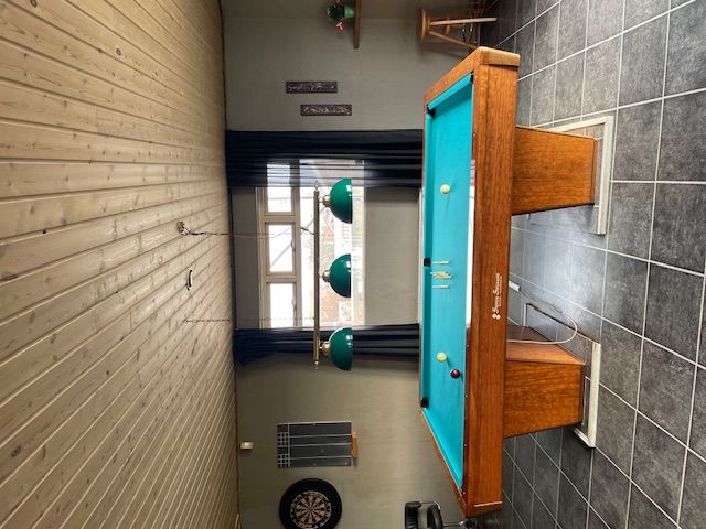 Billede af en poolborte i stuen med tre grønne lysekroner og en træstol bagved